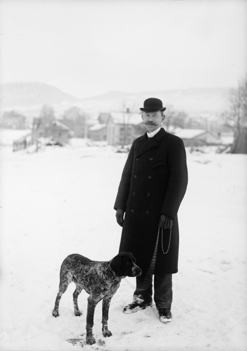 Mann med hund står ute i snøen, antatt på Skoletorget