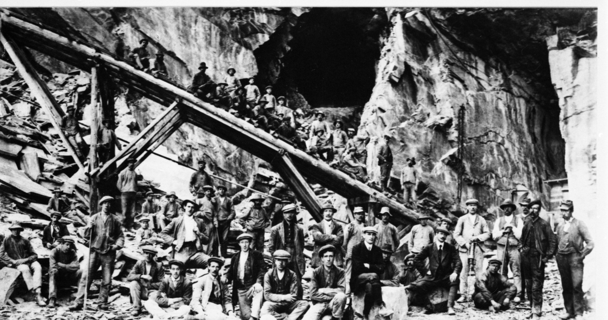 En stor gruppe menn samlet ved en av gruveinngangene ved Valdres Skiferbrud. Dette er mest sannsynlig arbeidskarer som jobbet ved skiferbruddet.