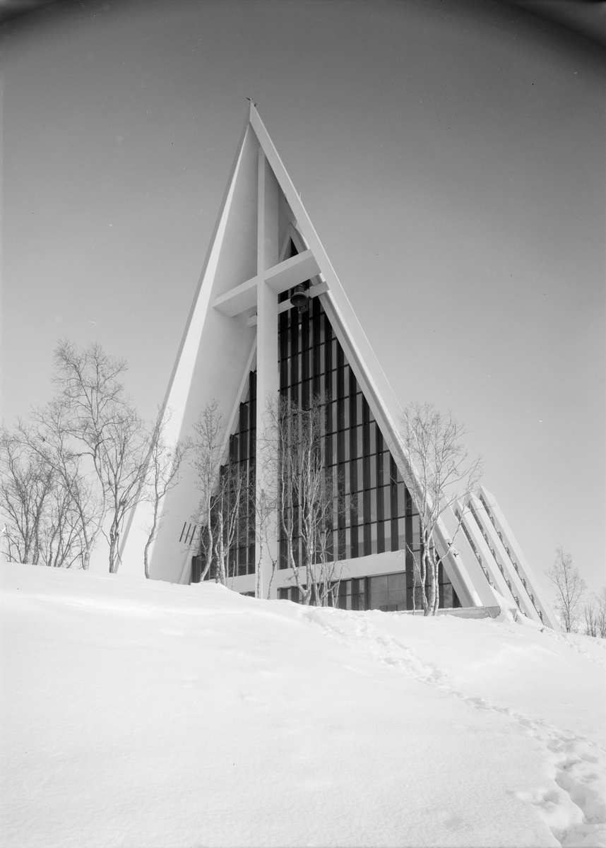 Arkitekturfoto av Tromsdalen kirke, bedre kjent som Ishavskatedralen. Med sitt avtrappede båthusformede eksteriør og sine åpne glassgavler er den blitt et landemerke i området. Kirken ble innviet 19. november 1965.