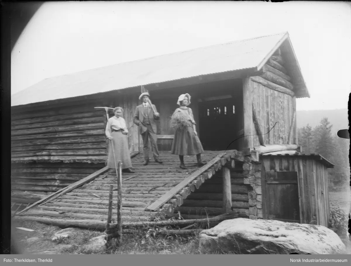 To kvinner og en mann stående på låvebru på Tovestul. En av kvinnene har rive i hånden, den andre har høy i armen og mannen har greip på skulderen.