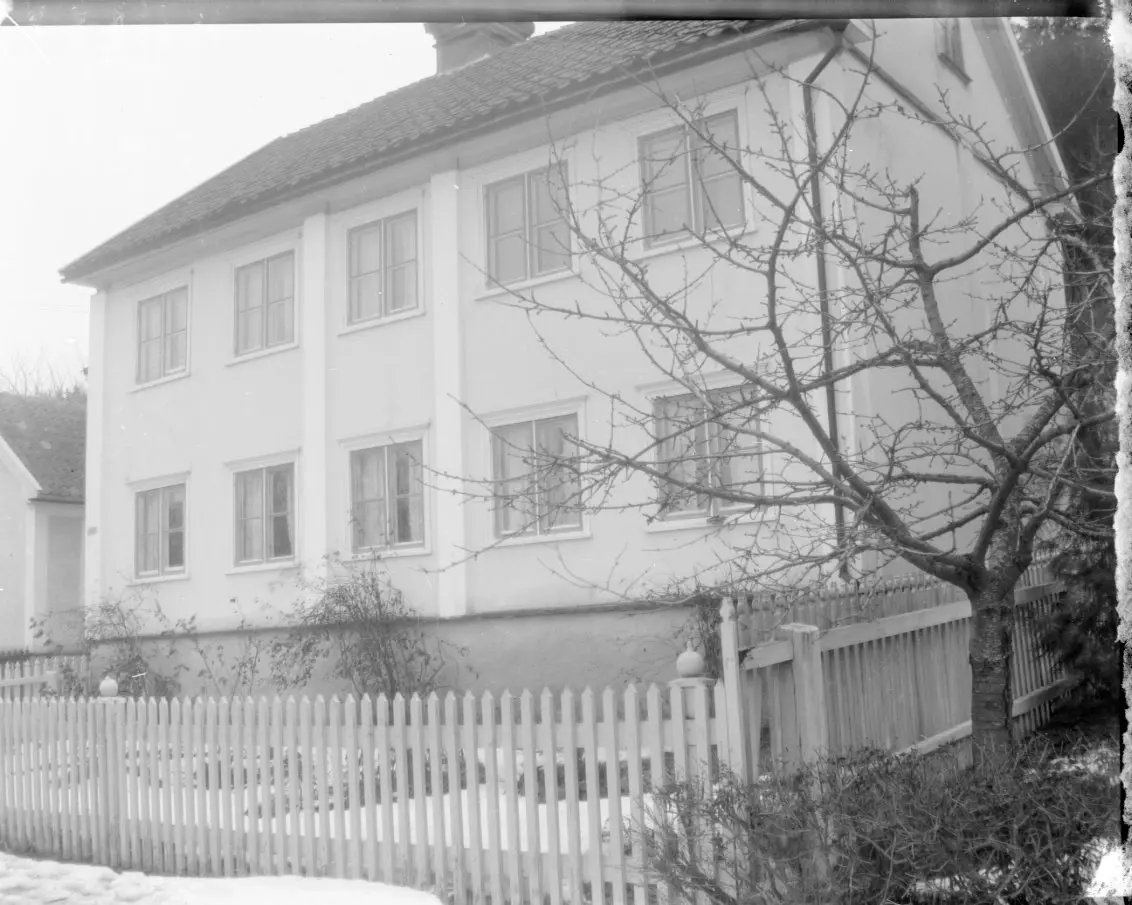 Ett putsat tvåvåningshus fotograferat från gatan utanför. Det ligger ...