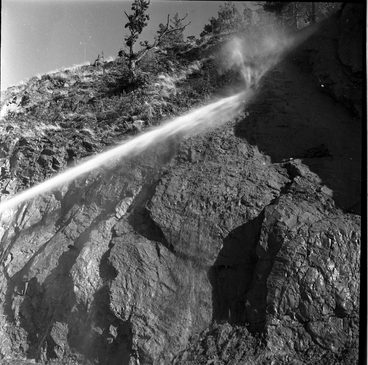 rasberget vid länsgränsen 1961. Närbild på en bergvägg och strålen från en vattenkanon som riktas mot toppen av bergväggen.