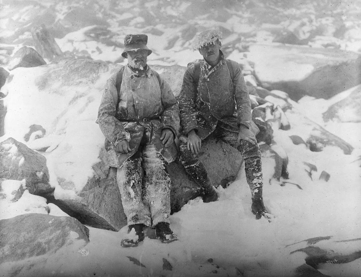 To menn tar en pust i bakken etter topptur i snøstorm på Snøhetta, Dovrefjell, Oppdal, Trøndelag, 16. juli 1915.