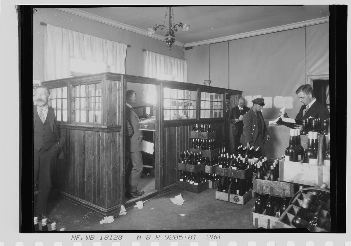 Flere menn står på et lager med vinflasker i kasser, Vinmonopolet. Fotografert 1924.