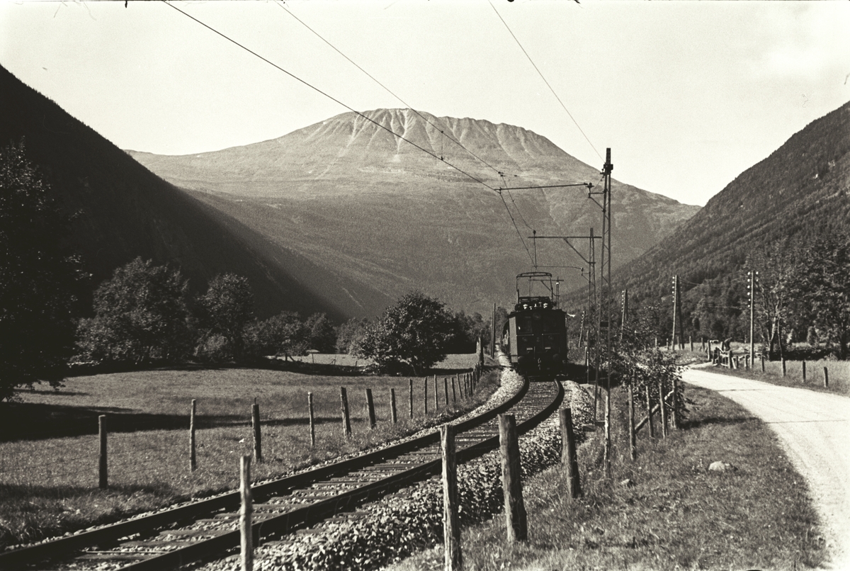 Toget på vei til Vestfjorddalen.  Veien på den ene siden og åker på den andre siden av sporet.