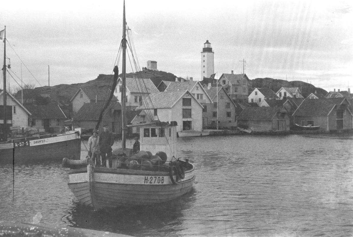 Fiskebåt på vei til kai med fangsten.  I bakgrunnen Kvitsøy fyr og bebyggelsen rundt.