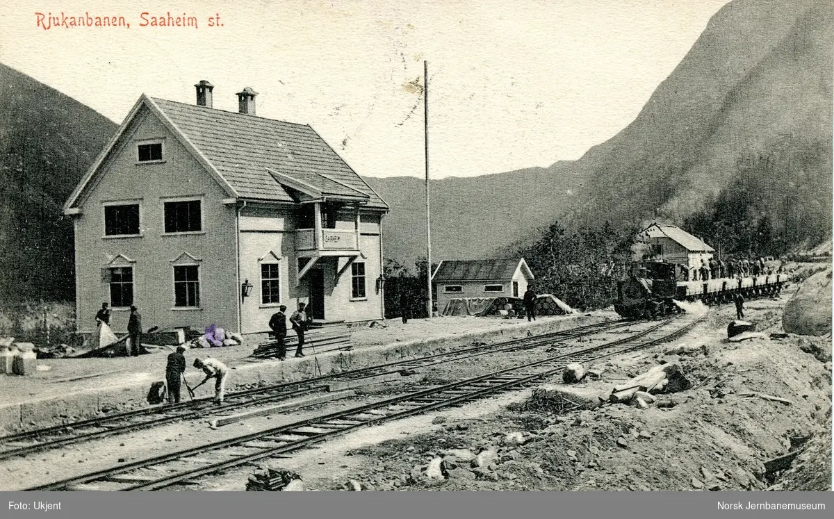 Rjukanbanens damplokomotiv ODIN med grustog og anleggsarbeidere kjører inn på Saaheim (Rjukan) stasjon