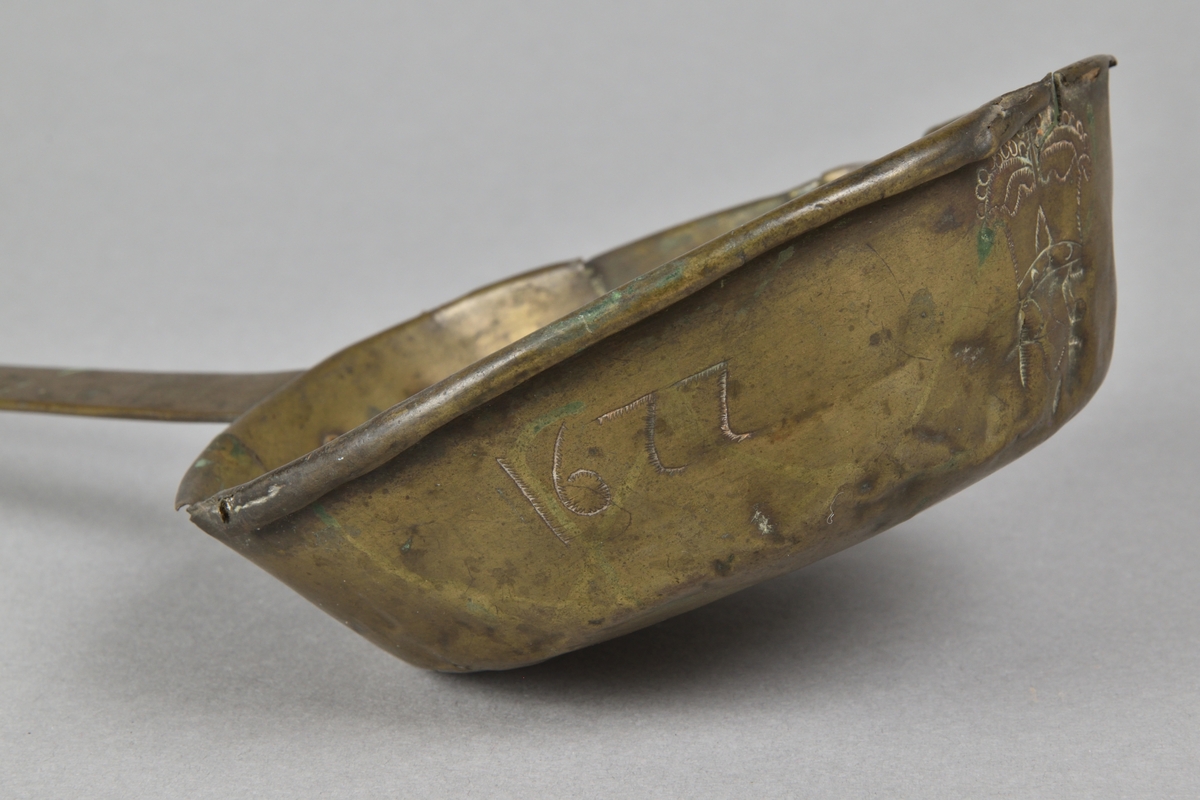 Skopa tillverkad i mässing. Cirkelrund skopa med snip och rullad överkant. Handtag fäst med nitar. Med graverad ornering i form av en krona över initialerna "RSE", samt graverat årtal "1677" och initialerna "I D".