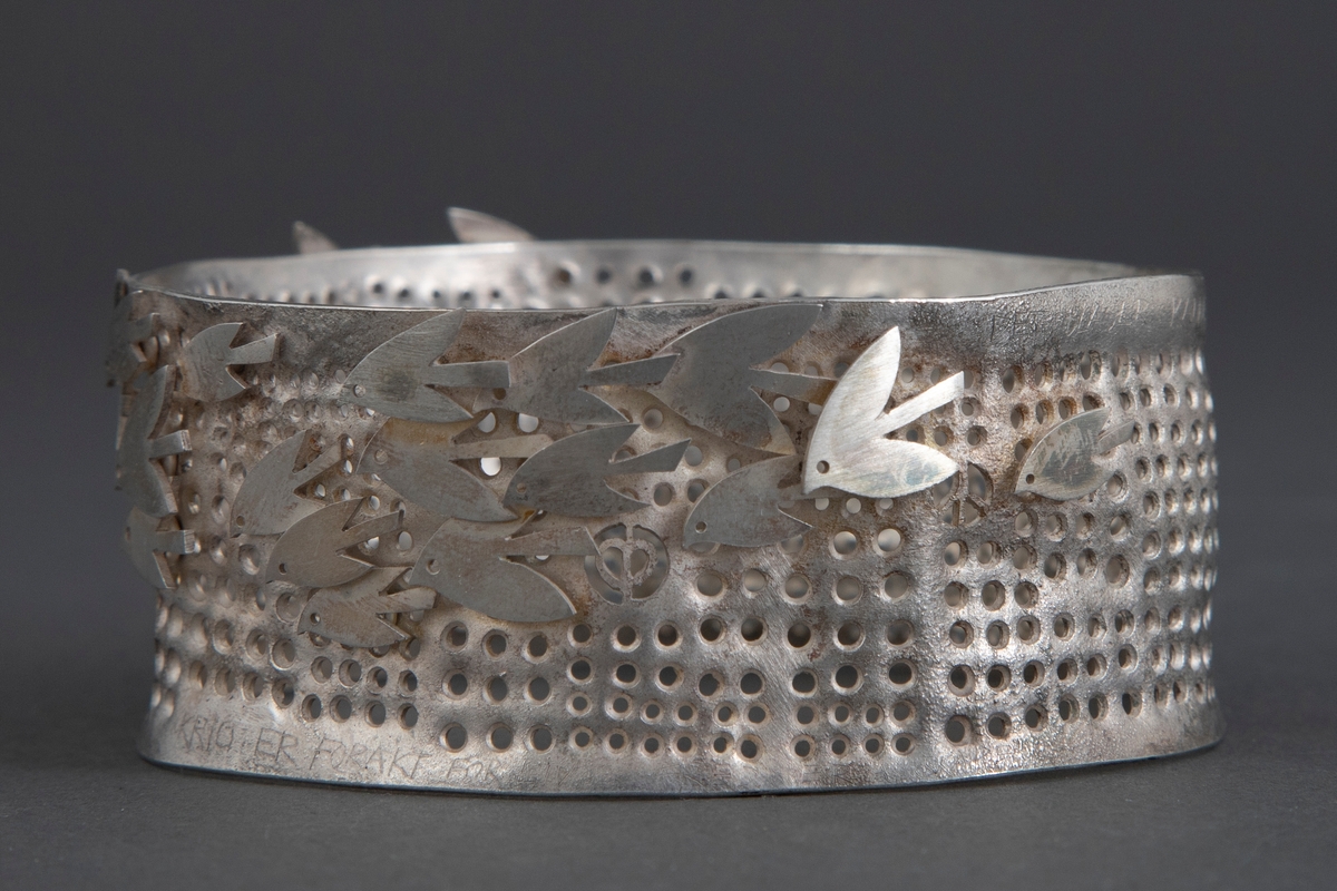 Tilnærmet sirkulær armring i sølv. Overflaten er perforert, og dekorert stiliserte fugler.