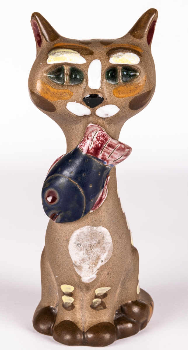 Figurin i form av katt med en liten fisk i munnen,  brunfärgat lergods med glaserade detaljer. Formgiven av Dorothy Clough för Gefle Porslin 1955.