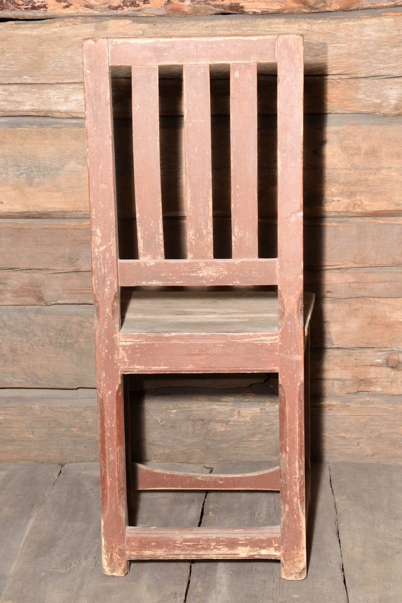Stol tillverkad i trä, rödmålad. Rektangulär ryggbricka, delvis genombruten med tre spjälor. Enkel ostoppad sits. Stolen står på fyra raka ben, med delvis fasade hörn. Benen nederst sammanhållna med fyra stabiliserande slåar.