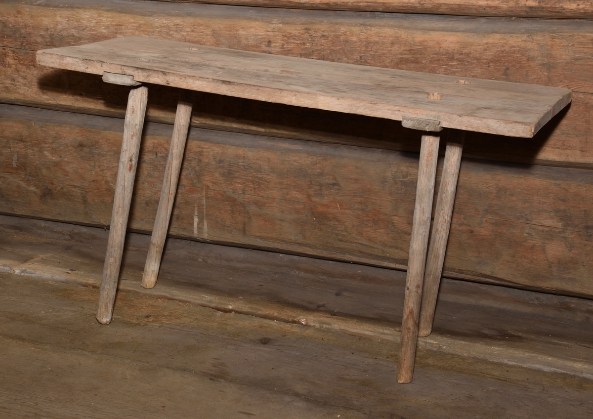 Bänk tillverkad i trä. Med enkel rektangulär sits på fyra utåt snedställda ben. 