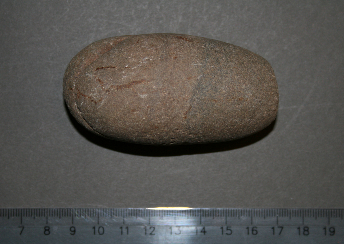 Naturlig stein i mellomstor mandelpotetstørrelse med bruksspor i begge ender. Den ene enden er blitt plan etter intensiv bruk.