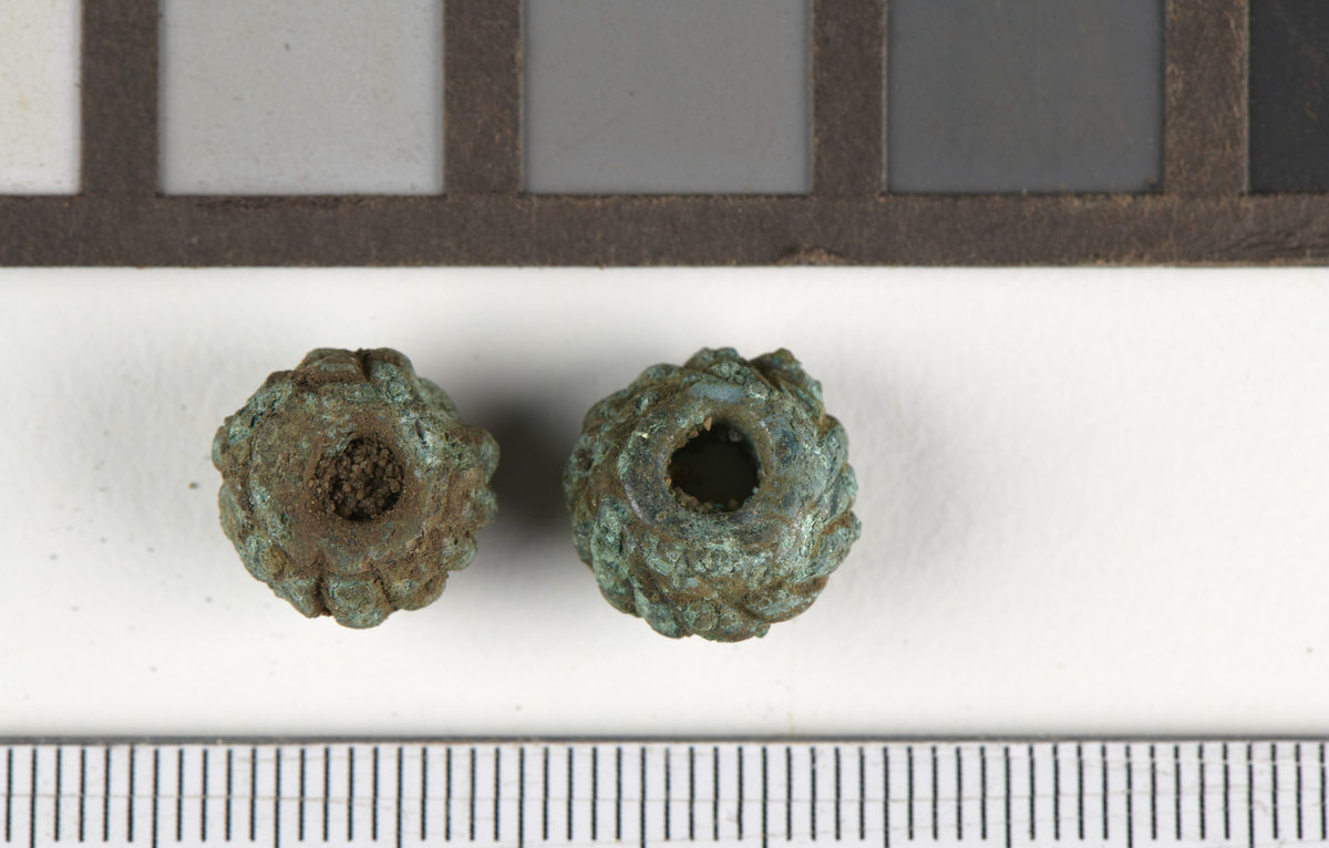 To perler i kobberlegering, sannsynligvis bronse. Begge perlene er runde, med vertikale riller på utsiden. Som Tempelmann- Mączyńskas form 529, men typen kan ikke dateres presist.