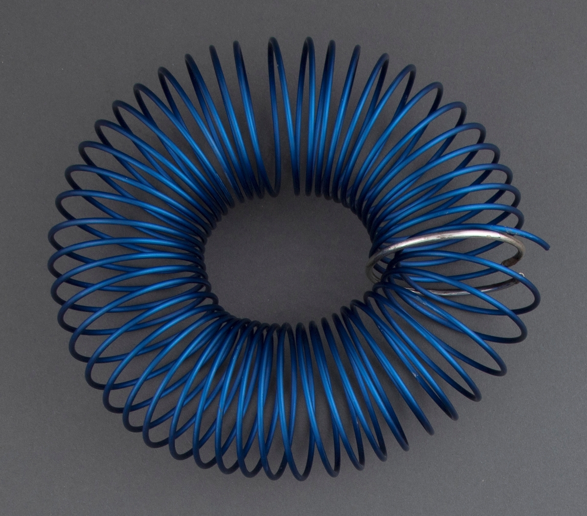 Armsmykke satt sammen av en spiral av blått eloksert aluminium. Ett ledd i spiralen er uført i sølv. Smykket er mykt og føyer seg etter håndleddet, men beholder samtidig sin form.