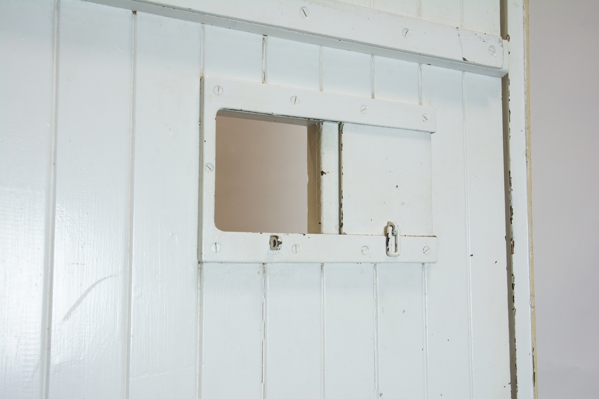 Arrestdörr i trä. Låsmekanism av enklare slag. "Besiktningslucka" i dörren som skjuts åt sidan för att kunna se in i fängelsecellen.