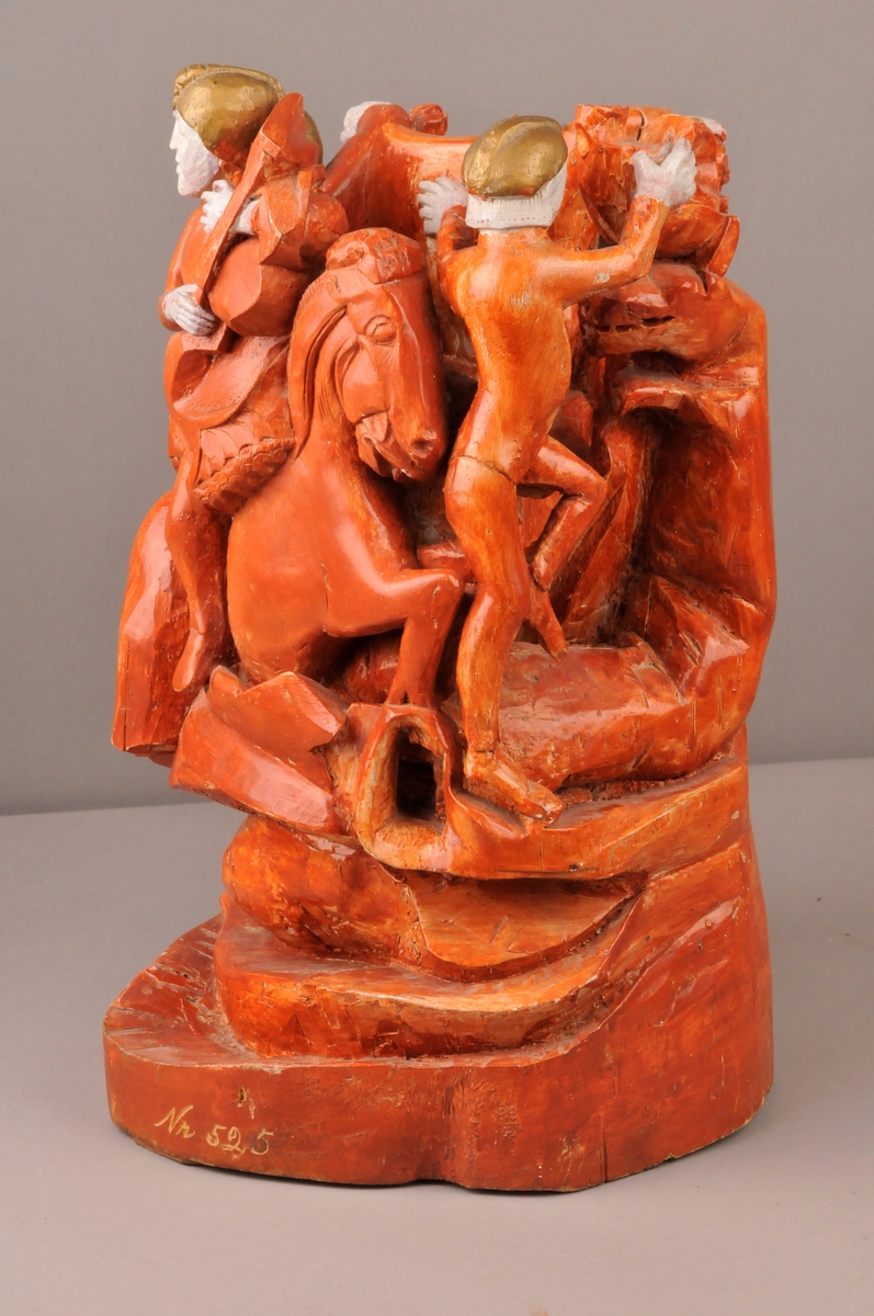 Skulptur av 4 riddere rundt ein kubbe og 4 dyrefigurer. Raud farge, ridderene har bronsefargede hjelmer, kvite ansikt og hender. Nede på foten av skulpturen er det innskripsjon.
