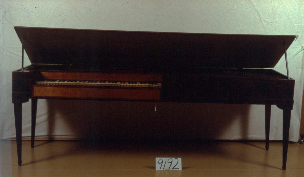 Klavikord, rektangulär, brunmålad låda med kannelerade ben med hörnkonsoller. Runt klaviaturen intarsia av lönn och mahogny. Heltoner av elfenben, halvtoner av ebenholts. Tillverkad av Kraft MP instrumentmakare, Stockholm.