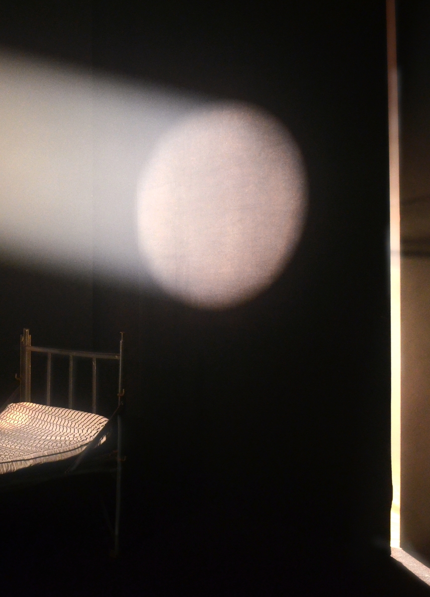 Et mørkt rom med en seng og et sirkelformet lys som treffer veggen. Fotografiet er en del av serien Isolasjon fra skjermet avdeling for demente på et sykehjem i Oslo.