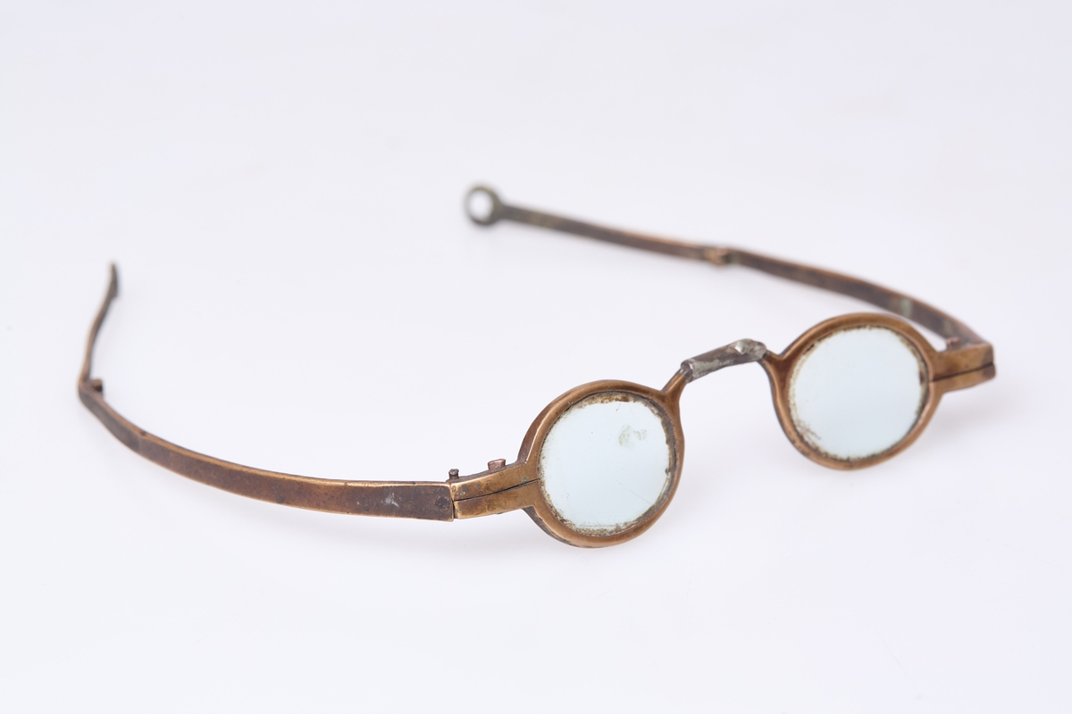Brille med små ovale glass og grov innfatning. Flate stenger med ledd som ytterst har et rundt hull