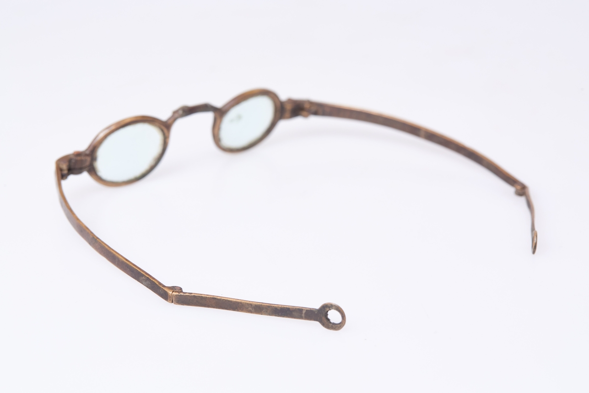 Brille med små ovale glass og grov innfatning. Flate stenger med ledd som ytterst har et rundt hull