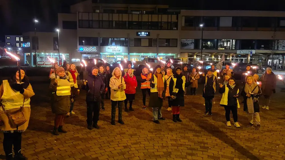 Fotografi av et fakkeltog. Mange mennesker står samlet. De holder tente fakler, og flere har på refleksvest. Fakkeltoget blir tatt bildet av ved Kongsvinger stasjon. Menneskene ser inn i kameraet.