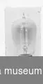 Glödlampa, päronformad, upptill avslutad i en spets. Handblåst av klart glas med gängad metallsockel (Edisonsockel). Mitt i lampan en glasstång och metalltrådar (glödtråd, av volfram?). Längd: 12,5 cm.