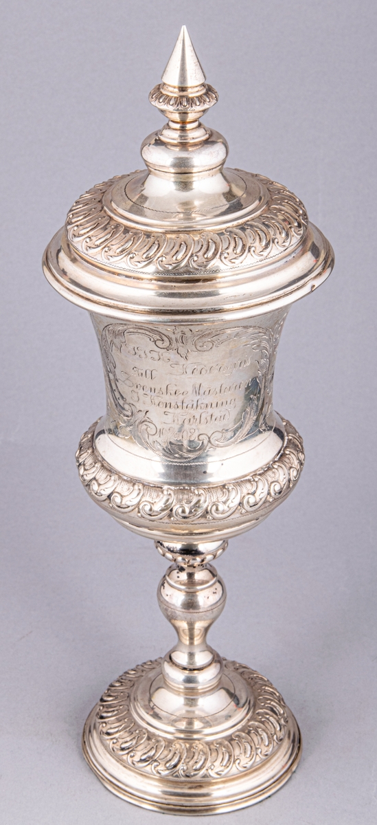 Pokal med lock, av silver. Stämplad: CGH, O, C7 (1905).
Inskription: IFK Hederspris till svenske mästaren i konståkning Karlstad 9/2 1908.