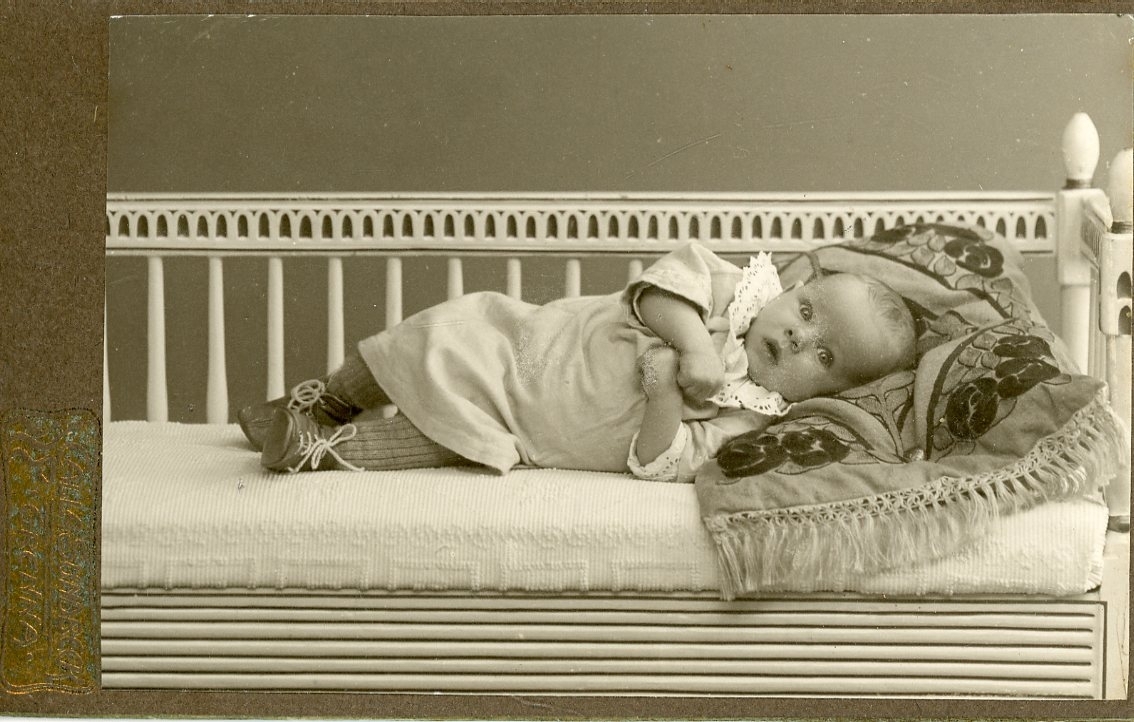 Kabinettsfotografi av ett spädbarn som ligger på en kudde på en soffa.