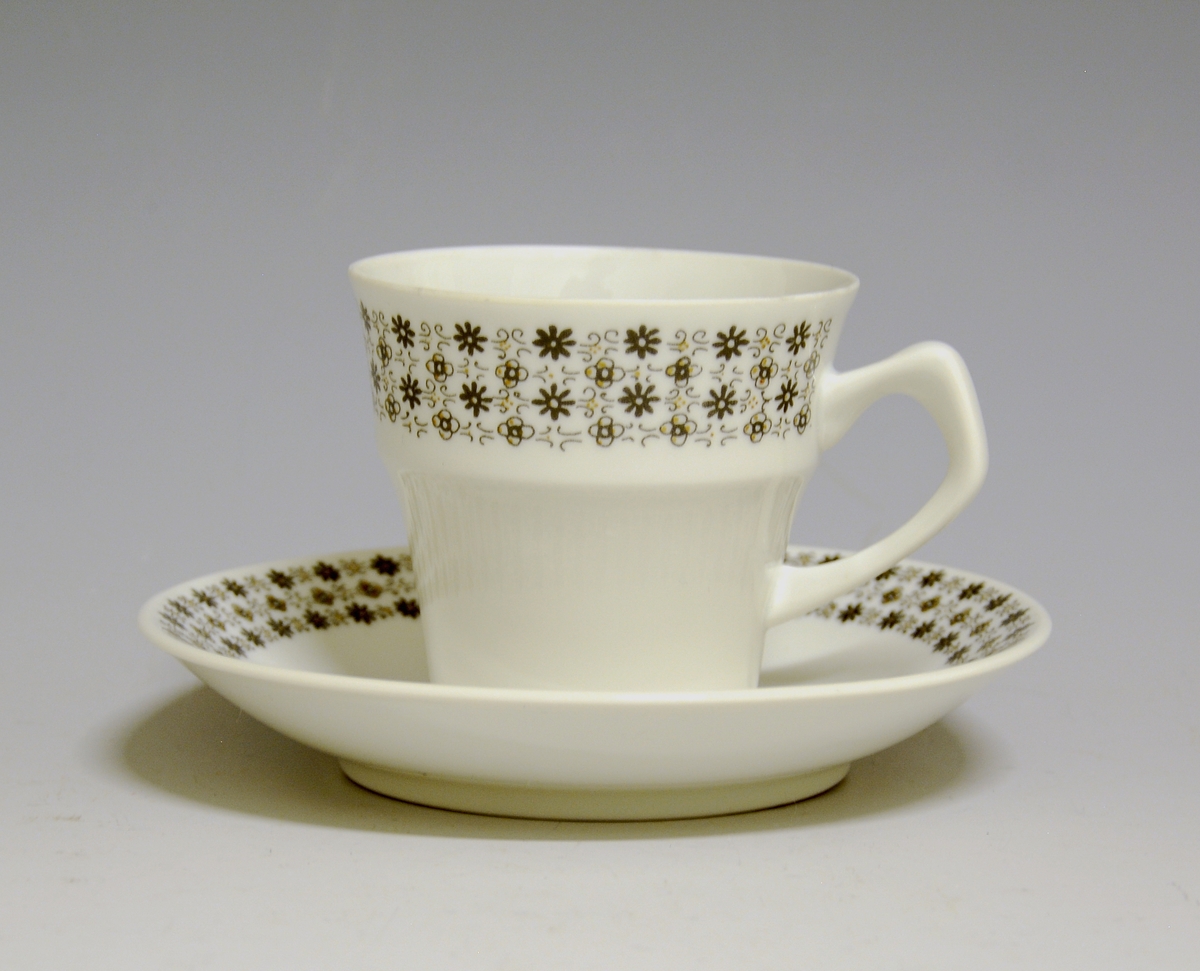 Kaffekopp av porselen med hvit glasur og bord med småblomstret trykkdekor i sort og gull i øvre del av korpus.
Modell: Petita (eller variant av)
