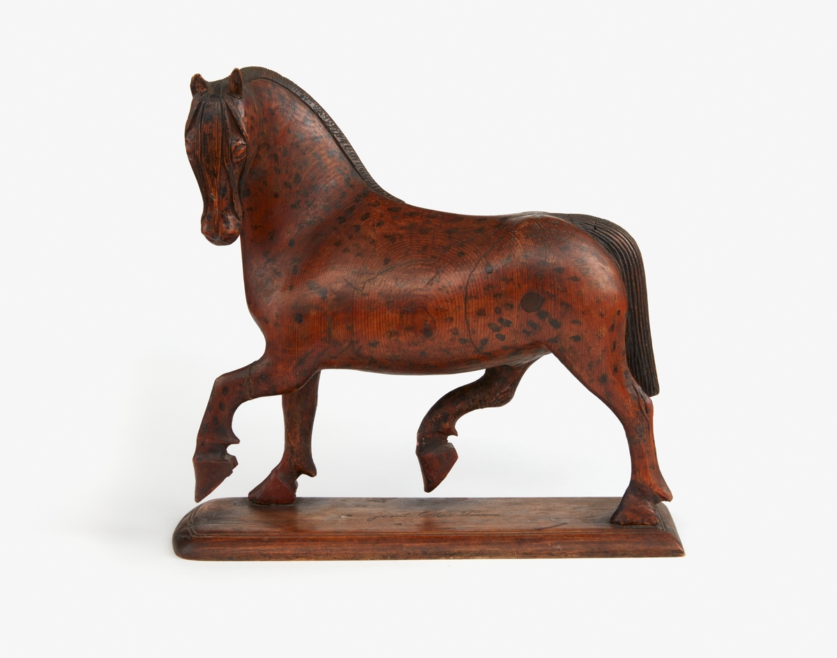 Hästskulptur med målning (fläckar) i brunt av Jemt Olov Persson Orsa. 

Längd: 321 mm.
Bredd: 118 mm.
Höjd: 304 mm.