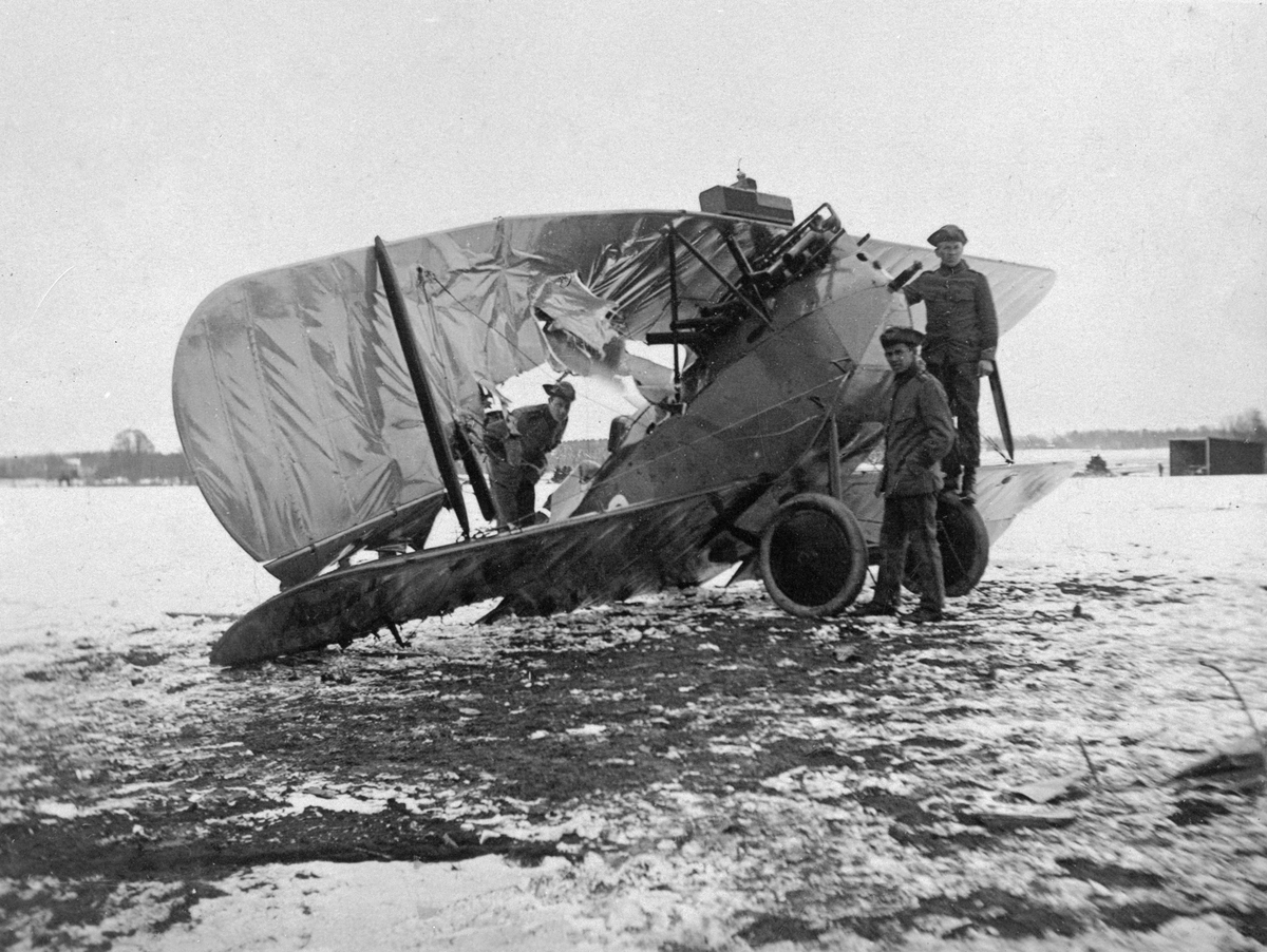 Flygplan J 1, Phönix D. II efter landningshaveri, vintertid, omkring 1930. Tre militärer vid flygplanet.