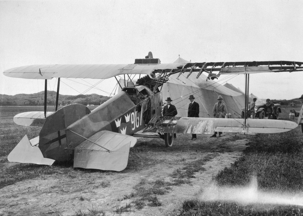 Brandskadat flygplan Phönix D.II nr 967, står på ett flygfält, 1923. Tälthangarer och människor i bakgrunden.