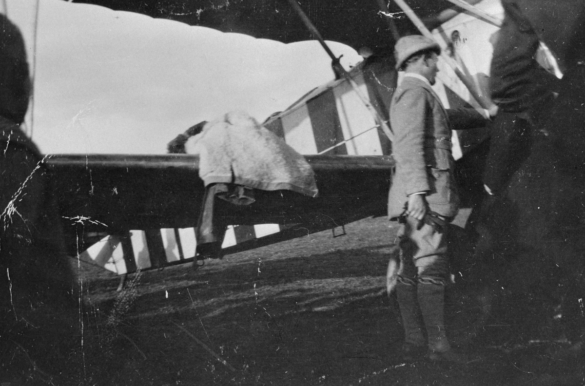 Flygplan Fokker D. VII, som flögs till Malmen 1919 av den tyske stridsflygaren Herman Göring, uppställt vid tälthangarer. Flygplanet övertogs av Flygkompaniet och fick nummer 937. Målning innan övertagandet. Mannen i ljus kostym är möjligen Göring.