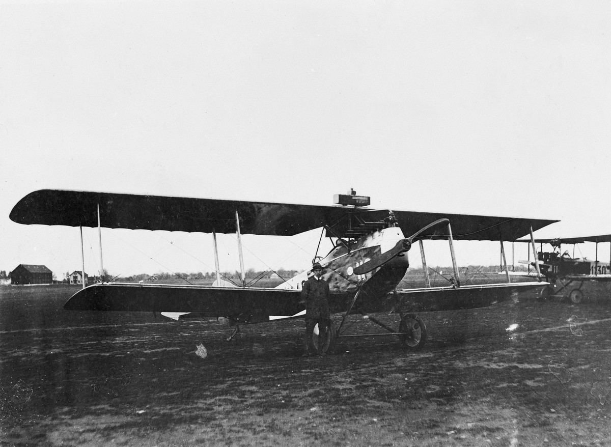Två flygplan FVM Albatros 160 uppställda på flygfältet på Flygkompaniet på Malmen, omkring 1922-1926. En man står vid ett av flygplanen. Röda och Gula förråden syns i bakgrunden.