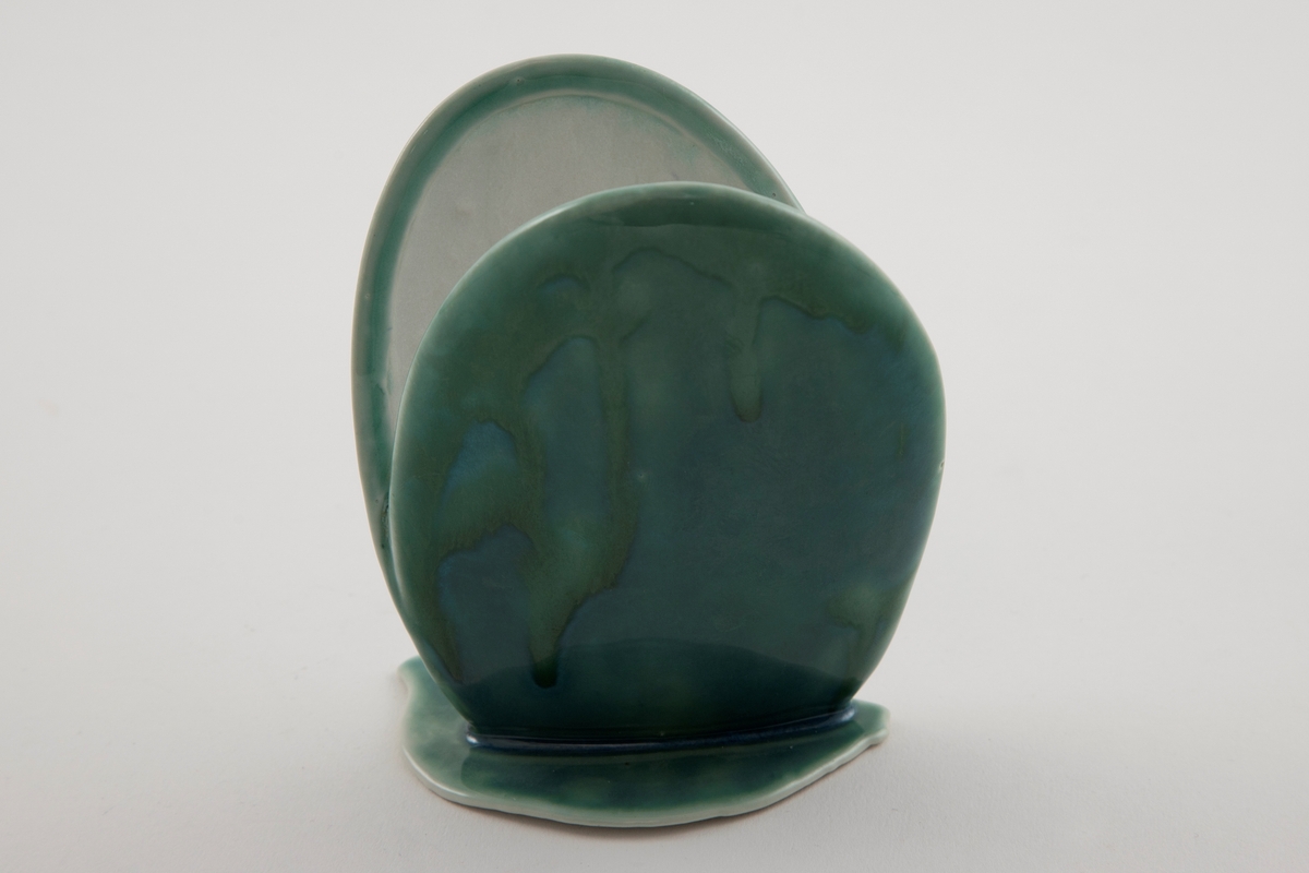 Porselensvase med en åpen skjell-lignende, stående form på flat sokkel med uregelmessige kanter. Turkis og grønn rennende glasur på utsiden, hvit glasur på innsiden.