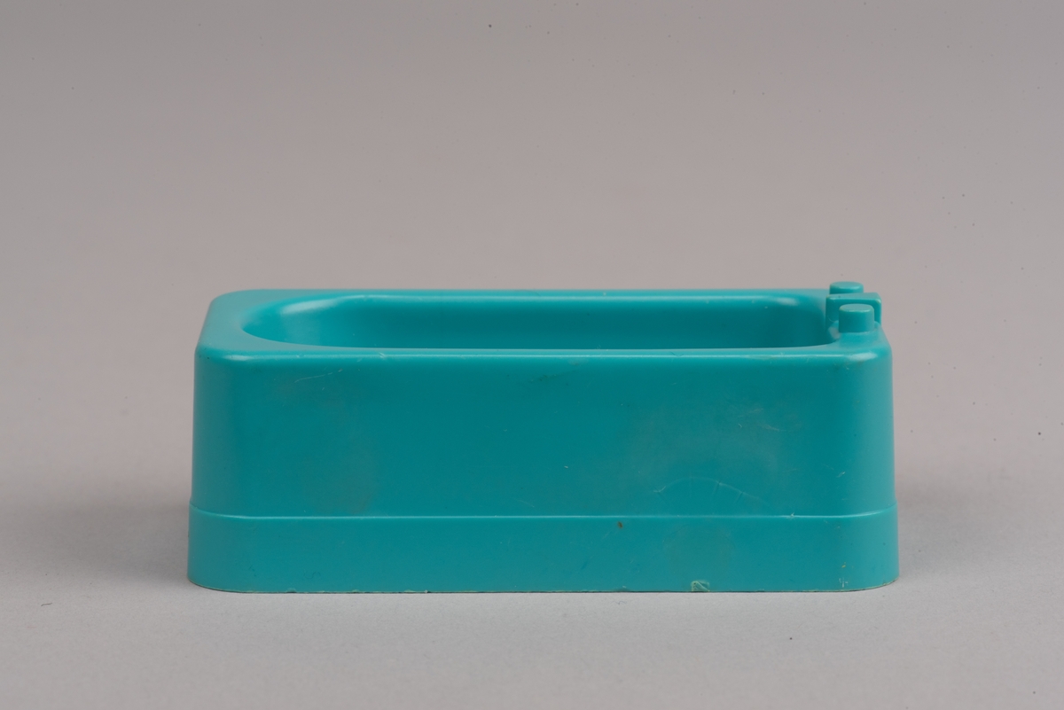 Dockskåpsmöbel i form av ett badkar tillverkat av plast.
Badkaret är rektangulärt i turkos färg. I botten finns ett avrinningshål och på den ena kortsidans övre kant sitter två kranar och en blandare, mycket förenklade i formen.