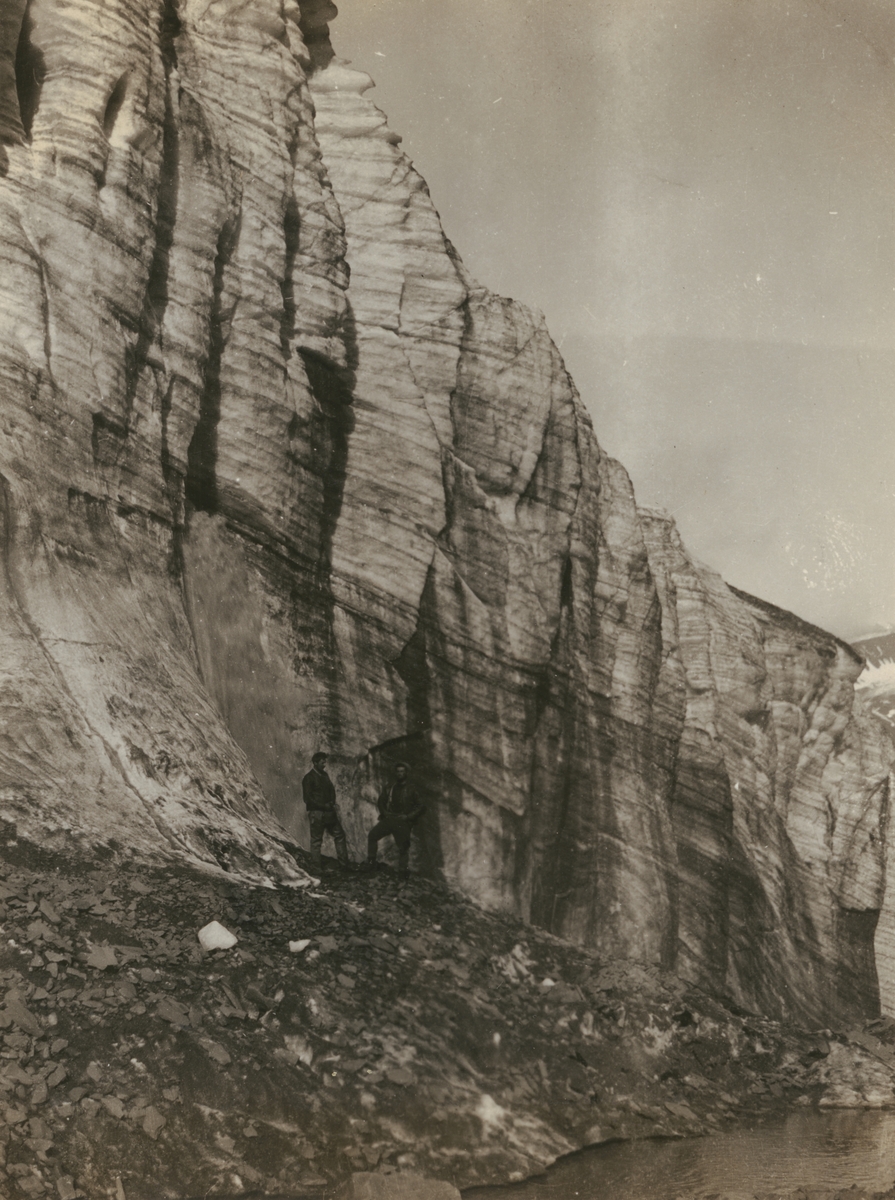 Fotografi från expedition till Sveagruvan. Motiv av två män som står nedanför ett berg.