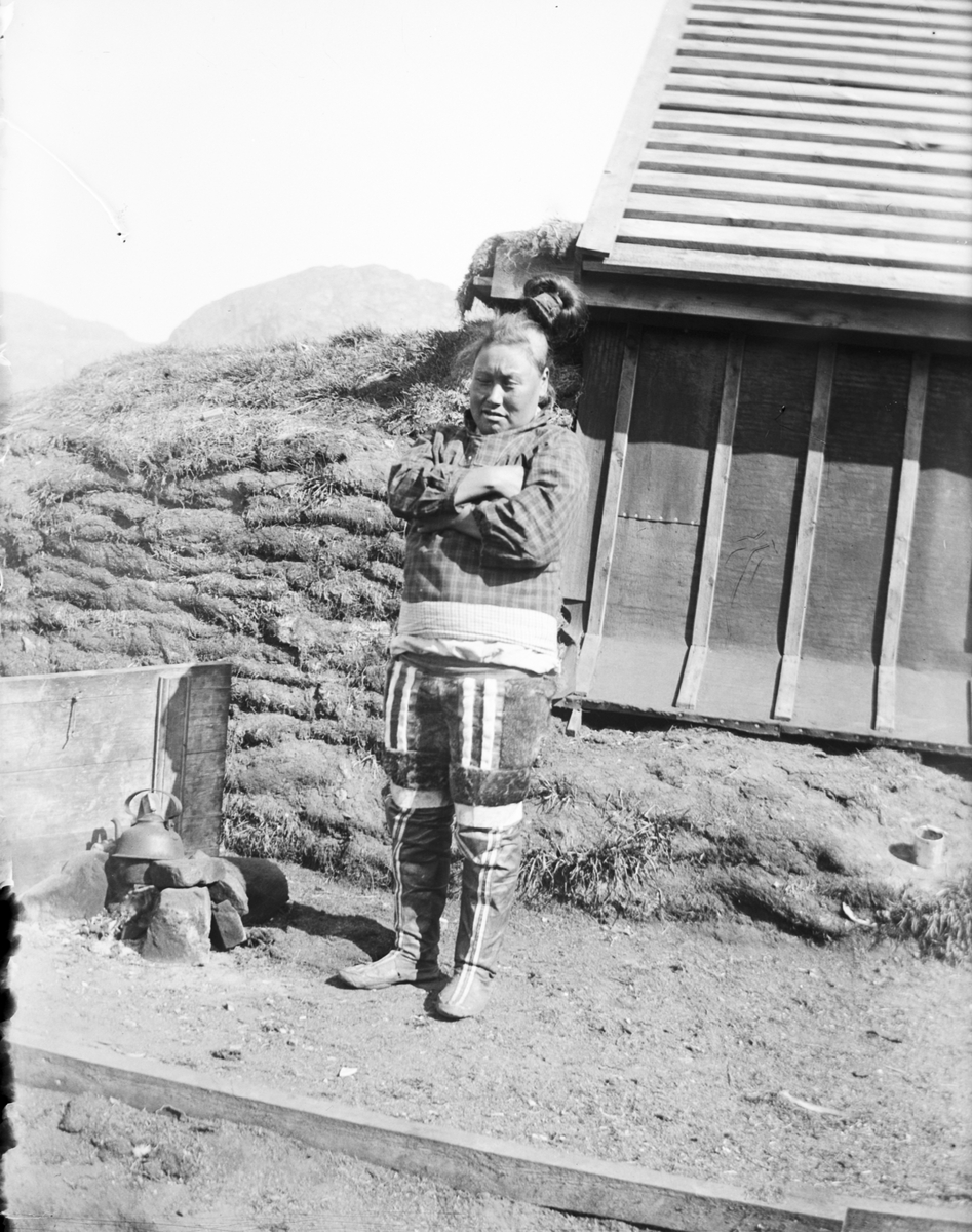 Fotografi från Grönland. Motiv av kvinna vid litet trähus.