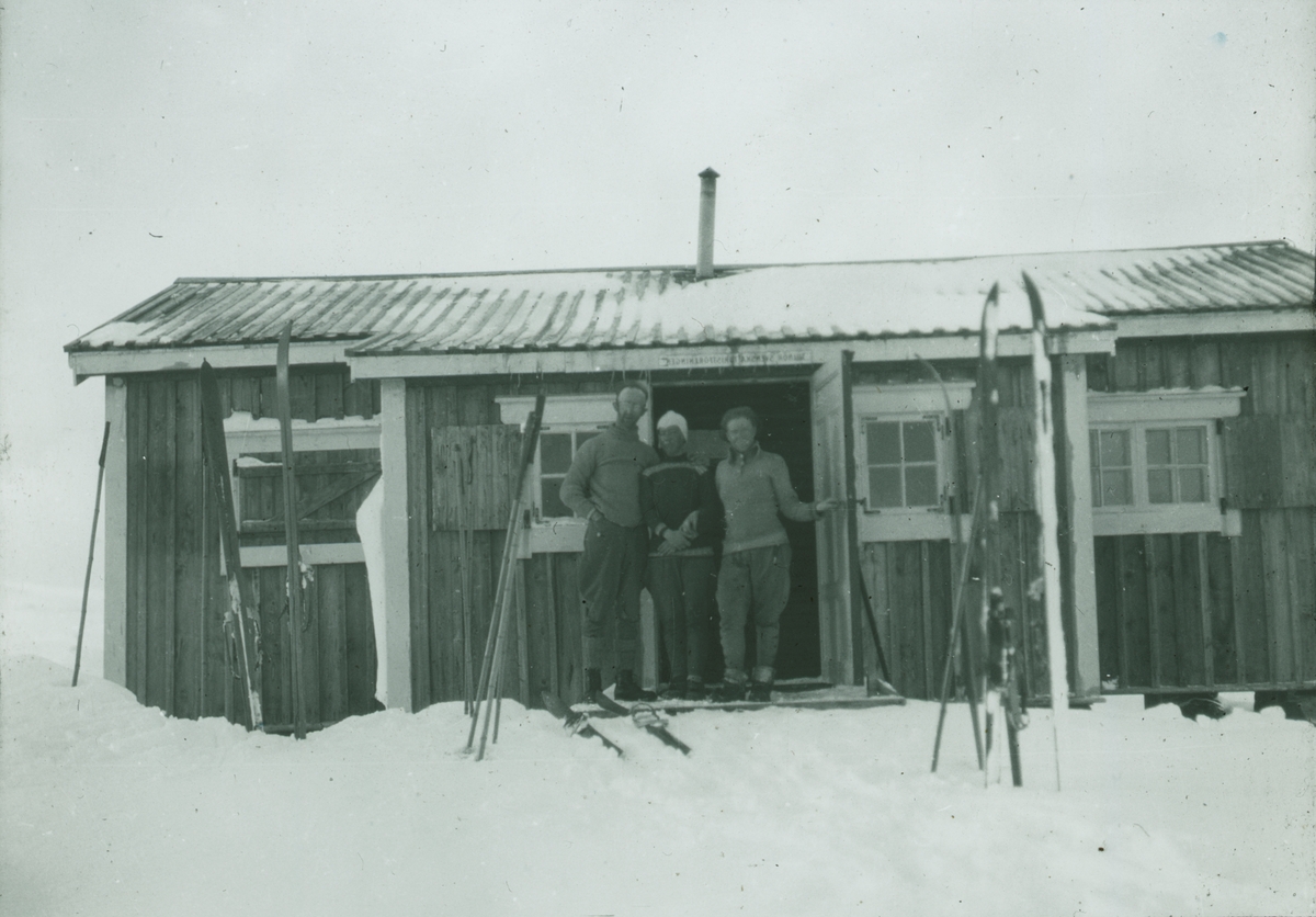 Fotografi från expedition till Spetsbergen. Motiv av familj framför hus i snö.