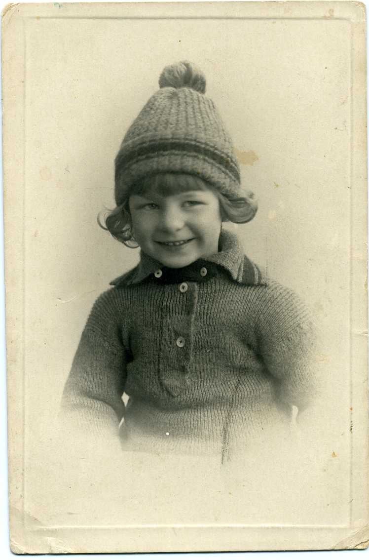 Porträtt av en liten pojke i stickad tröja och mössa i matchande mönster.