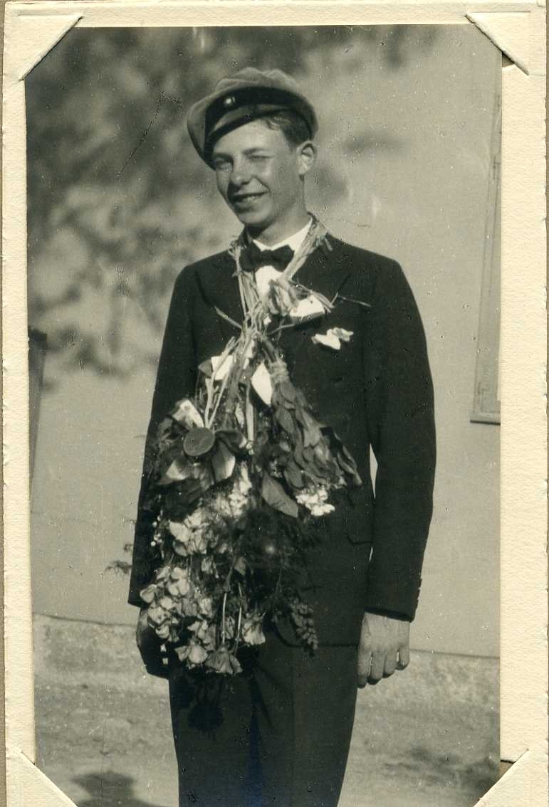 En ung man i abiturientmössa e motsv och blommor runt halsen.
Han kisar.