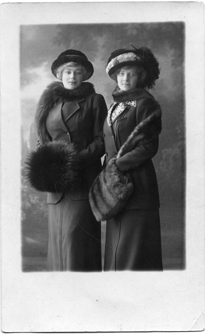 Två vinterklädda kvinnor med stora hattar och muff i en ateljé. Vykort