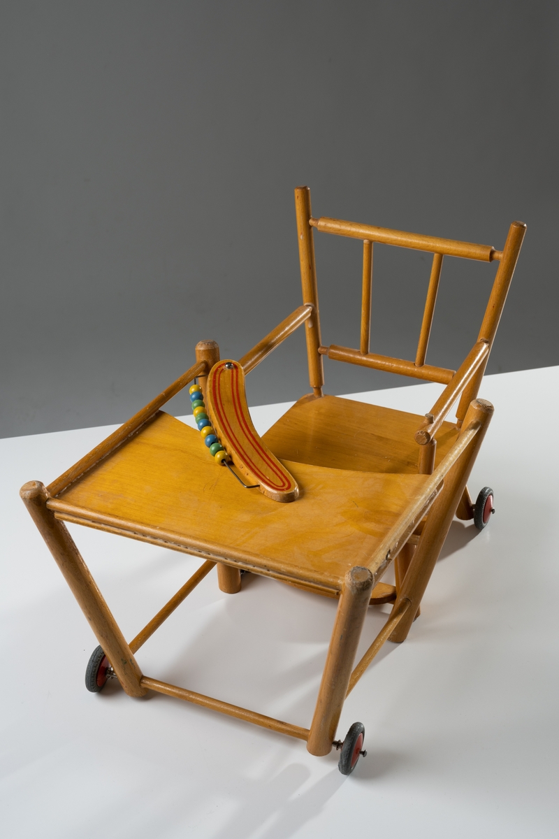 Barnstol till docka av naturfärgat och lackat trä. Stolen är delbar, kan dels vara hög (matstol), dels fällas ner till stol och bord, som går att rulla (lekstol). Pinnstolsmodell med svarvade pinnar i ryggstödet och armstöden samt fyrkantig sits. Framtill sitter en smal skiva med tio målade träkulor uppträdda på en metalltråd. Skivan går att fälla upp och ut. De fyra hjulen är av trä och gummi (har torkat).

Se vidare Historik
