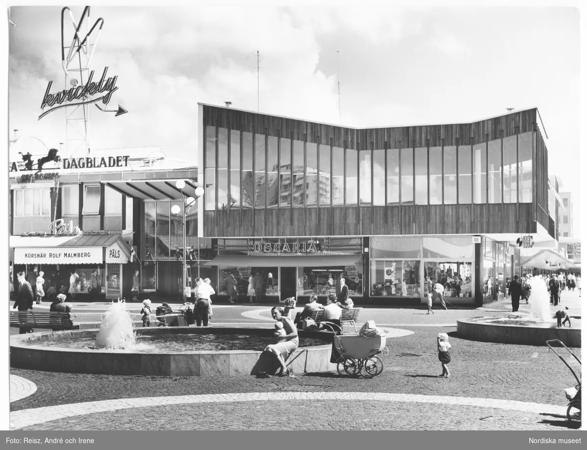 Stockholm. Vällingby torg, invigt 1954, med butiker "Päls, Körsnär Rolf Malmberg" samt "Oscaria" , Vällingby centrum. Folkliv.
