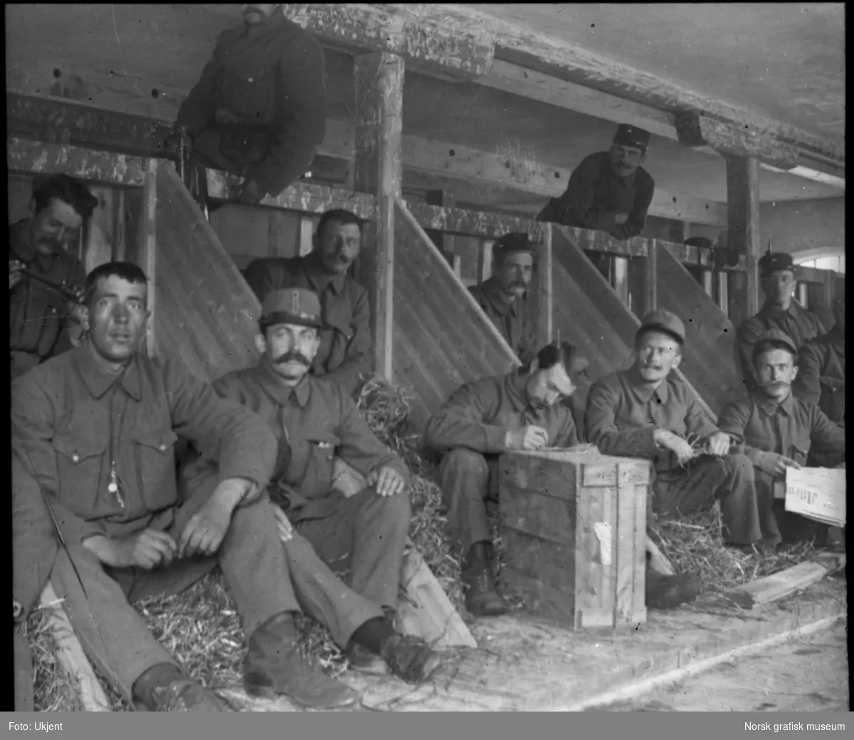 En gruppe soldater sitter i båsene til husdyr på ei låve.