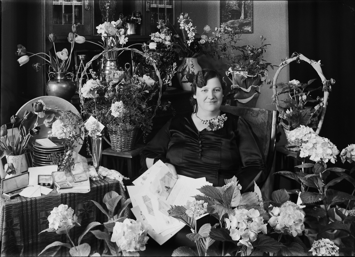 Kvinna i hemmiljö omgiven av blommor, Östhammar, Uppland