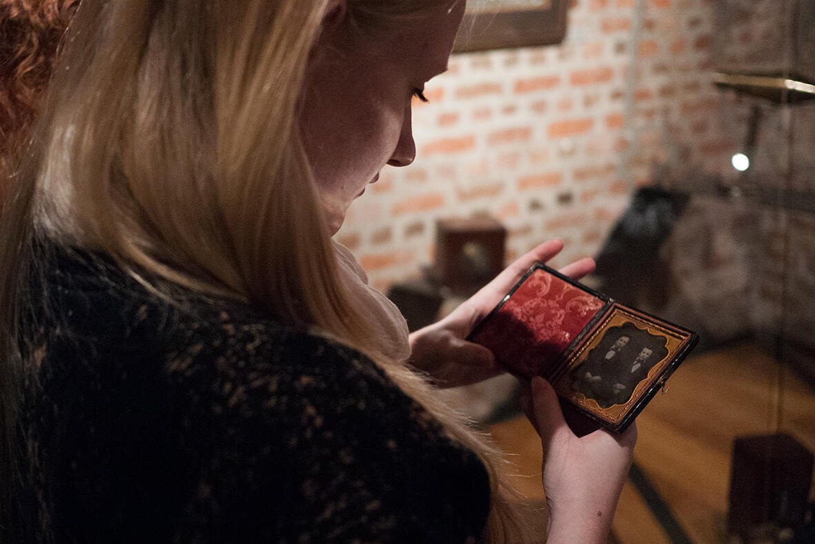 Jente ser på et daguerreotypi, et fotografi fra 1840-tallet som ligger foreglet i et etui med rød fløyel. Vi ser jenta halvveis bakfra. Fotografi fra utstillingslokalene til Preus museum.