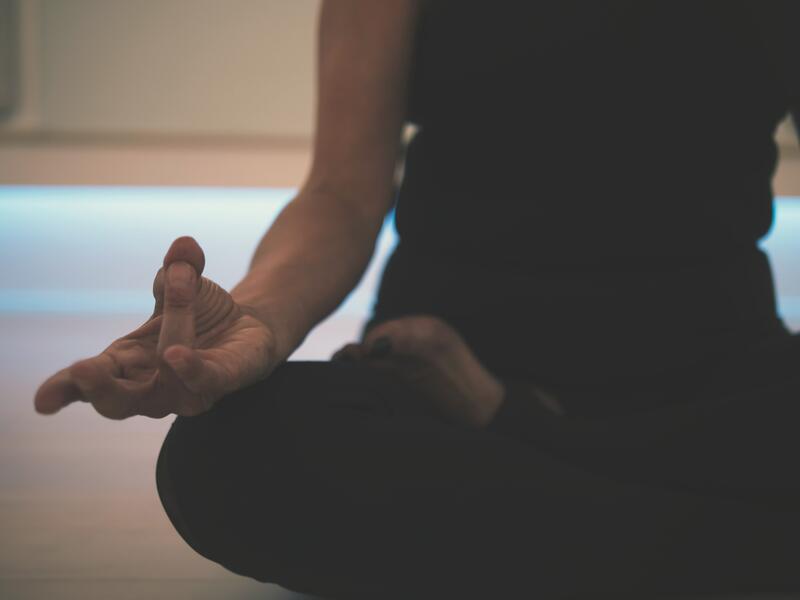 Bilde av en person som sitter i lotusstilling med svarte klær og hender i yogastilling på knær. Personen har svarte klær på, hodet er ikke synlig.