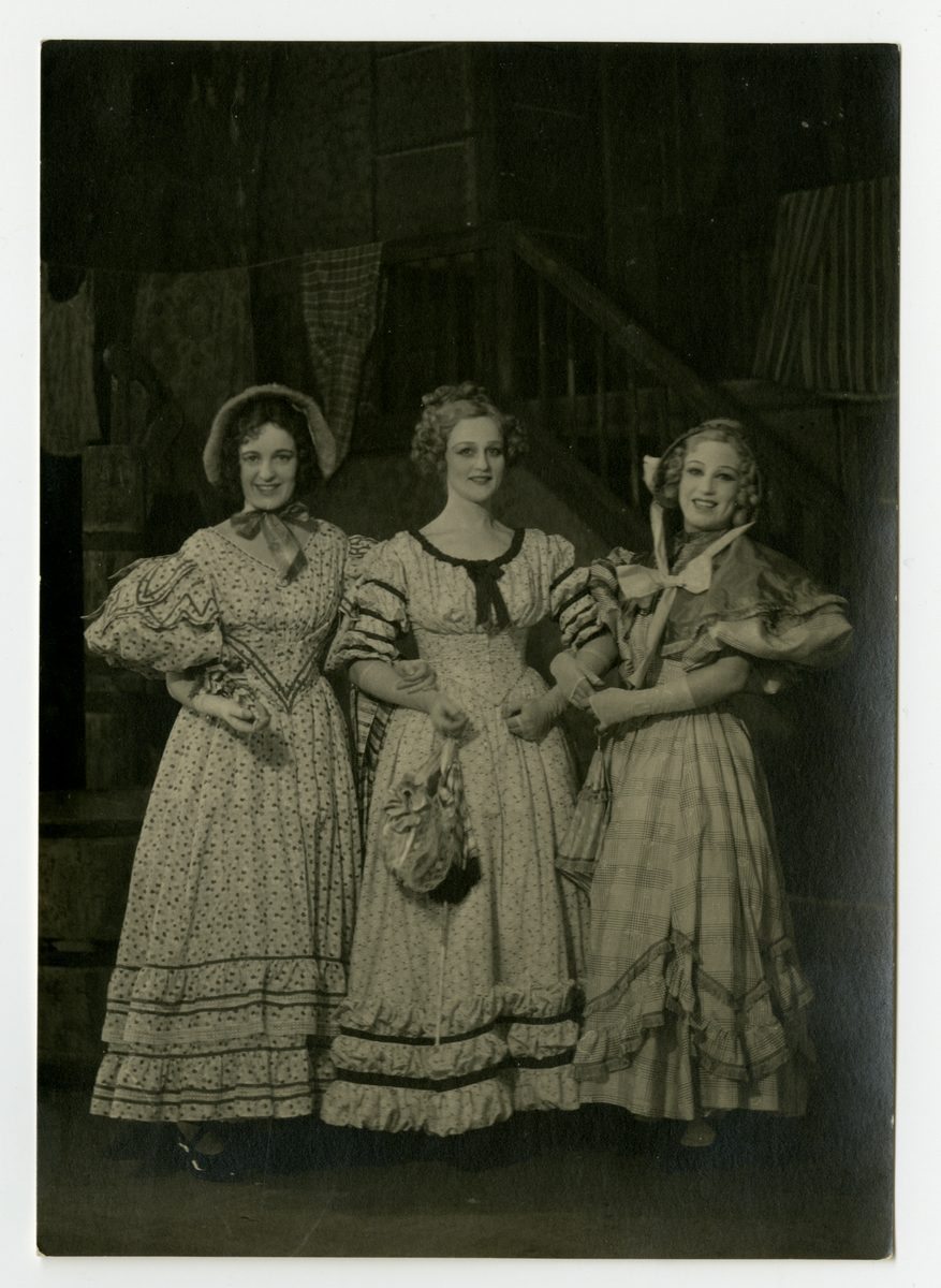 Tre kvinner i kostymer avbildet foran en teaterkulisse.